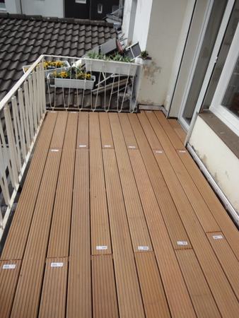Balkon mit neu verlegtem Holz-Terrassenboden, Geländer und Blumenkasten mit Blumen.