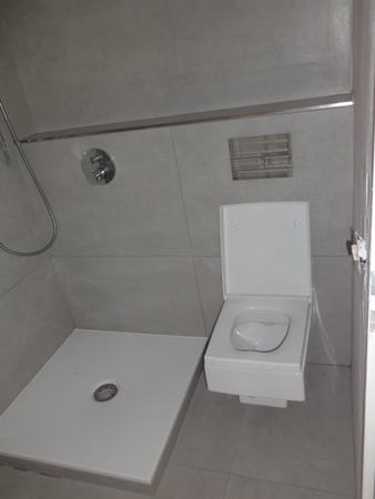 Barrierefreies Badezimmer mit bodengleicher Dusche und wandhängendem WC in modernem Design.