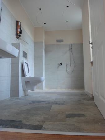 Barrierefreies modernes Badezimmer mit bodengleicher Dusche, Hänge-WC und Fliesenboden.