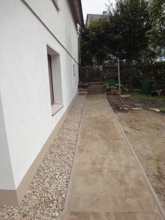 Gepflasterter Gartenweg neben modernem Haus mit Kiesstreifen und angrenzendem Grün.