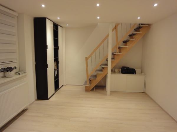 Modernes Wohnzimmer mit Holztreppe, Einbauschrank und hellem Laminatboden im Neubau.